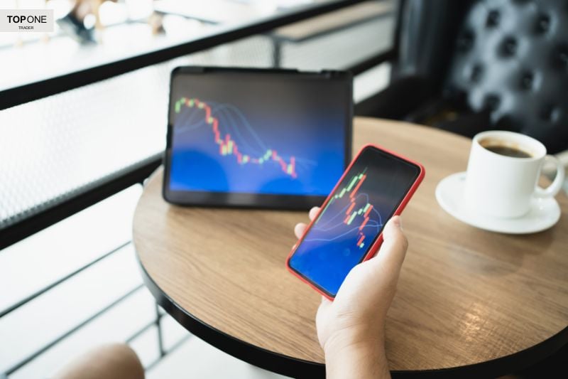 Trader monitoring stock market charts on phone and tablet, learning strategies on how to become a successful trader efficiently.