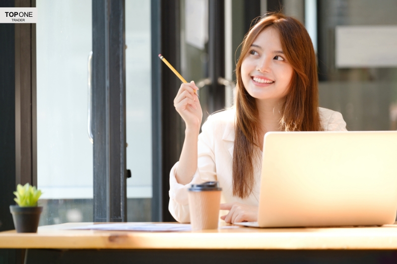 Smiling trader researching the cup and handle pattern on her laptop with a coffee nearby.